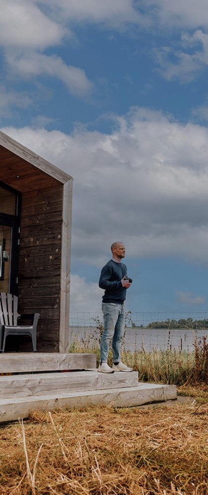 Man staat voor het Zuiderkrib Dijkhuisje met dijk en water in Kraggenburg, Flevoland