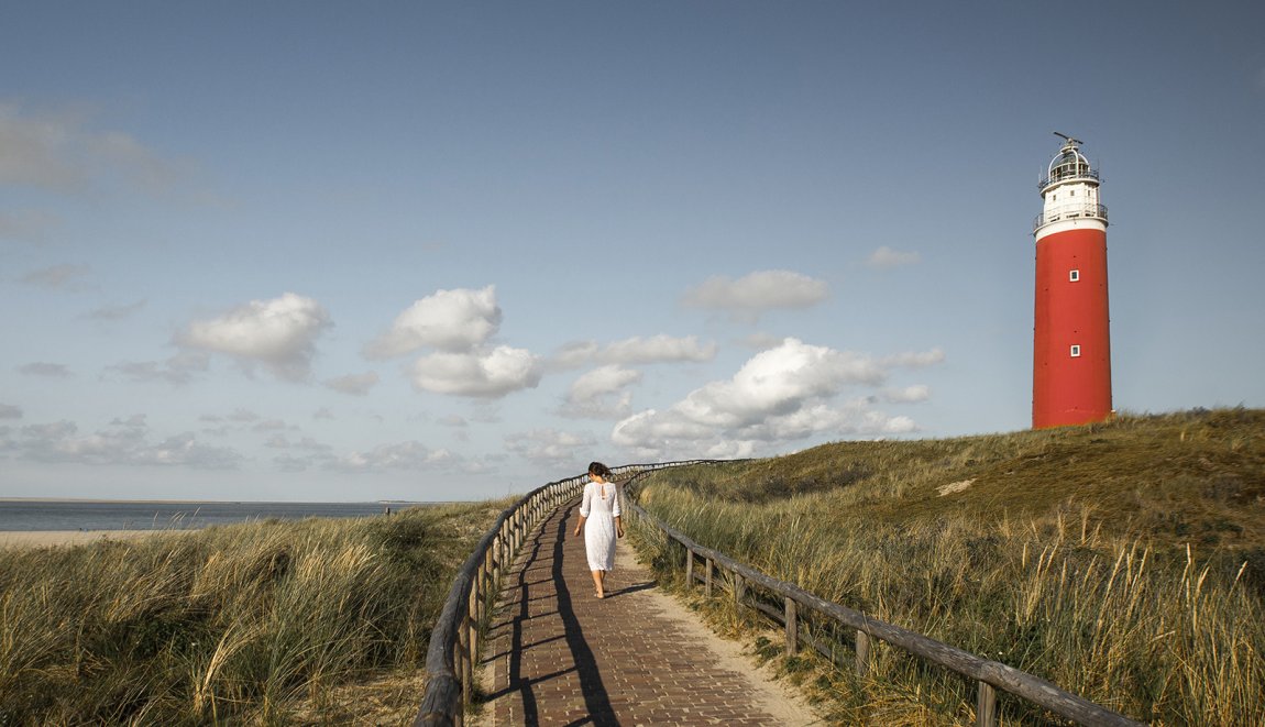 Vrouw loopt over pad bij vuurtoren van Texel in de zomer