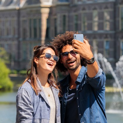 Vrolijk jong stel fotograferend bij de Hofvijver met zicht op de regeringsgebouwen