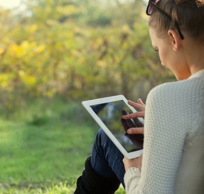Dame maakt  gebruik van tablet in het park zit tegen een boom