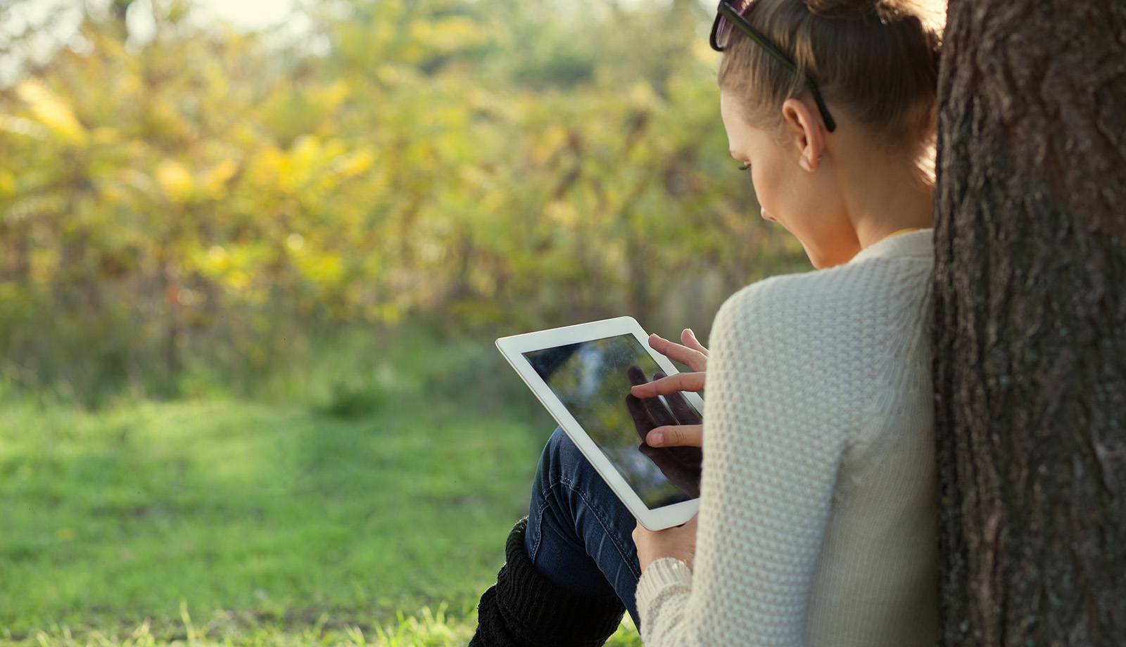 Dame maakt gebruik van tablet in het park zit tegen een boom Dame maakt gebruik van tablet in het park zit tegen een boom