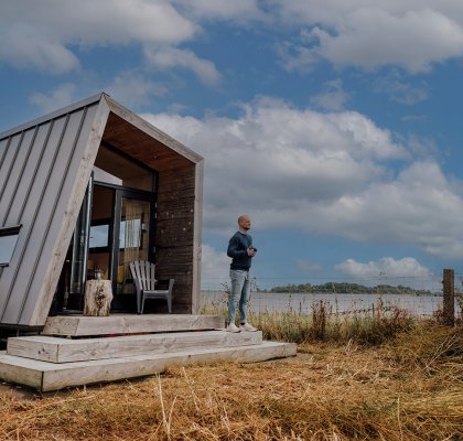 Man staat voor het Zuiderkrib Dijkhuisje met dijk en water in Kraggenburg, Flevoland