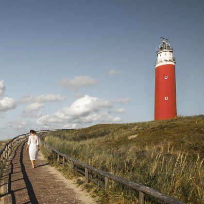 Vrouw loopt over pad bij vuurtoren van Texel in de zomer